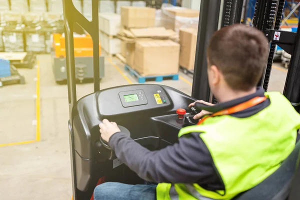 Storehouse medewerker in uniform werkt aan vorkheftruck in modern automatisch magazijn. De dozen liggen op de planken van het magazijn. Opslag, machineconcept. Logistiek in stock. — Stockfoto