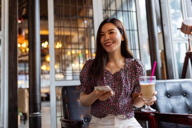 Cafe 'de cep telefonuyla konuşan, iş programını yöneten, toplantı planlayan, müşteri veya arkadaşlarıyla konuşan, modern kafeteryadaki masada oturan Asyalı kadınlar.