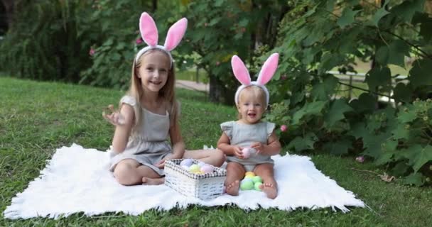 Tavşan Kulaklı İki Çocuk Bahçede ya da Parkta Paskalya Yumurtası Avı 'nı boyarken. Beyaz tatlı bir bebek ve kız kardeşi arka bahçede birlikte vakit geçiriyorlar. Yavaş çekim — Stok video