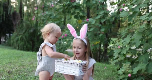 Двое детей с кроличьими ушами во время окрашивания пасхальных яиц в саду или парке. Милый белый ребенок и сестра проводят время вместе на заднем дворе. Медленное движение — стоковое видео
