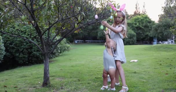 Två barn bär kaninöron när Pick Up målade påskägg jaga i trädgården eller parken. Söt kaukasisk bebis och syster spenderar tid tillsammans på bakgården. Långsamma rörelser — Stockvideo