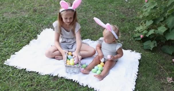 Two Children Wearing Bunny Ears when Pick Up painted Easter Egg Hunt In Garden or park. Cute caucasian baby and sister spending time together on backyard. Slow motion — Stock Video