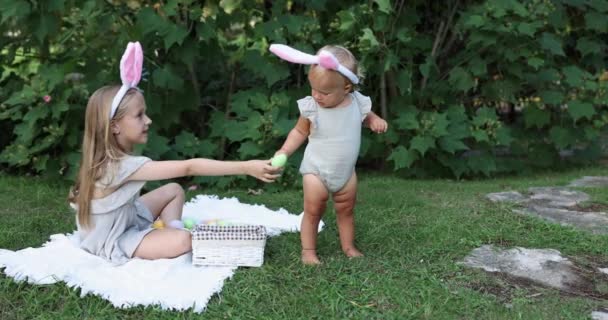 Δύο παιδιά που φορούν αυτιά λαγουδάκι όταν pick up ζωγραφισμένα πασχαλινό αυγό κυνήγι στον κήπο ή πάρκο. Χαριτωμένο καυκάσιο μωρό και αδελφή να περνούν χρόνο μαζί στην πίσω αυλή. Αργή κίνηση — Αρχείο Βίντεο