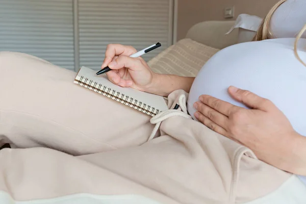 Een jonge zwangere vrouw die een koffer pakt voor een kraamkliniek thuis, close-up. Checklist voor de bevalling. Zwangerschap tijdens de coronavirus covid-19 pandemie — Stockfoto