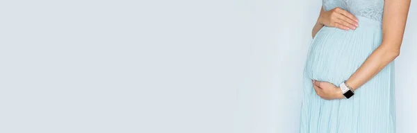 Fotografía de cerca de la joven mujer tocando las manos de su gran vientre en vestido azul pastel Aislado sobre fondo blanco con espacio de copia. Cuidado de la piel con crema hidratante contra las estrías. Emocional Imágenes de stock libres de derechos