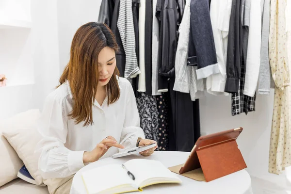 Starta småföretag, Ung kinesisk kvinna Företagare som använder smartphone eller surfplatta ta emot och kontrollera inköp på nätet för att förbereda förpackning produkt låda. online-försäljning koncept Royaltyfria Stockbilder