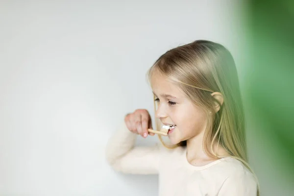 Söt liten flicka som håller hand eco bambu tandborste på beige bakgrund. Begreppet hållbart boende. Rädda planeten för våra barn Stockbild