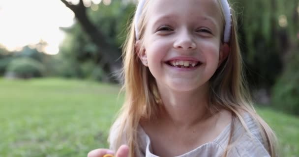 Close up emotional portrait of caucasian smiling teen girl with blonde hair seven years old. Funny cute child in summer park on sunset. Happy kid having fun when looking at camera — Stock Video