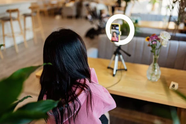 Sonriente mujer asiática transmitiendo en la cafetería moderna y utilizando la lámpara de anillo y el teléfono móvil — Foto de Stock