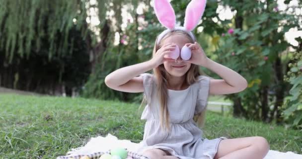 Adorable girl Wearing Bunny Ears when Pick Up painted Easter Egg Hunt In Garden or park. Cute caucasian child seven years old on backyard. Slow motion — Stock Video