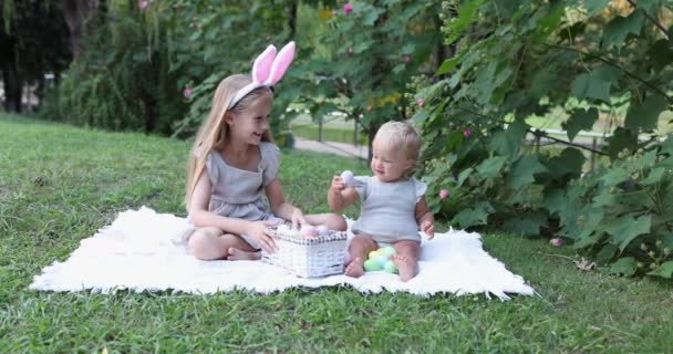 Duas crianças vestindo orelhas de coelho quando pegar pintado Easter Egg Hunt In Garden ou parque. Bebê caucasiano bonito e irmã passar tempo juntos no quintal. Movimento lento — Vídeo de Stock