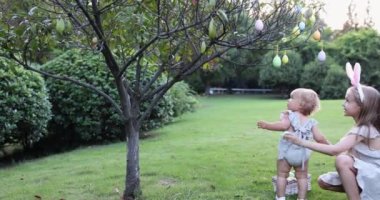 Tavşan Kulaklı İki Çocuk Bahçede ya da Parkta Paskalya Yumurtası Avı 'nı boyarken. Beyaz tatlı bir bebek ve kız kardeşi arka bahçede birlikte vakit geçiriyorlar. Ağır çekim. Yüksek kalite 4k görüntü