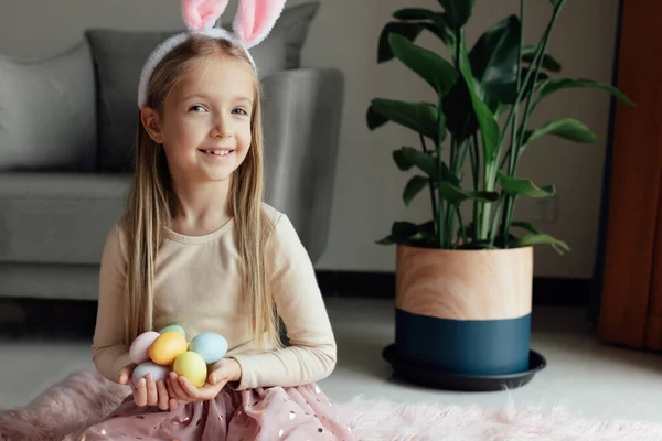 Niña caucásica feliz niño de ocho años en casa en la sala de estar con huevos de Pascua de colores. Permanecer en casa durante la pandemia del Coronavirus covid-19 — Foto de Stock