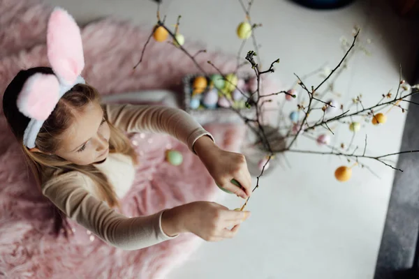 Glad kaukasiska småbarn flicka åtta år gammal hemma i vardagsrummet med färgade påskägg. Stanna hemma under Coronavirus covid-19 pandemi — Stockfoto