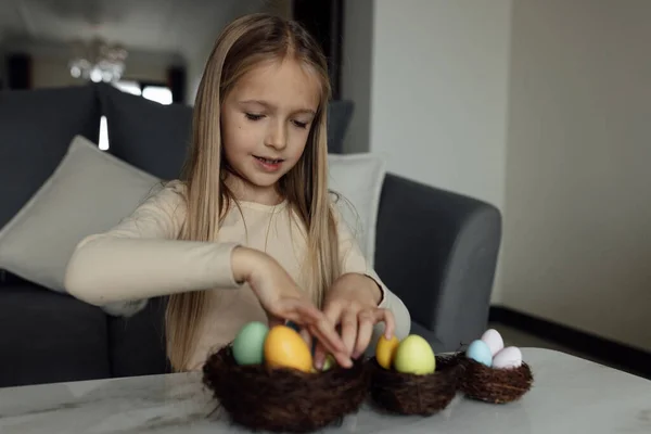 Niña caucásica feliz niño de ocho años en casa en la sala de estar con huevos de Pascua de colores. Permanecer en casa durante la pandemia del Coronavirus covid-19 — Foto de Stock