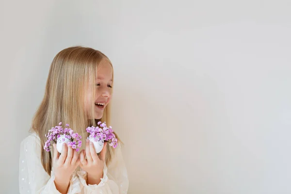 Joyeux enfant caucasien fille de sept ans tenant la main Oeufs de Pâques mignons avec des visages dessinés et couronne violette florale — Photo