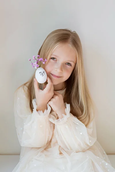 Szczęśliwy biały dzieciak dziewczyna siedem lat trzymając ręce słodkie pisanki z rysowane twarze i kwiatowy fioletowy wieniec — Zdjęcie stockowe