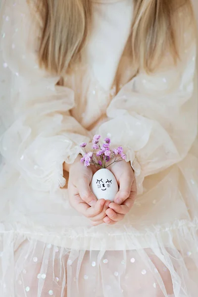 Feliz niña caucásica de siete años de edad cogidos de la mano Lindos huevos de Pascua con caras dibujadas y floral corona púrpura —  Fotos de Stock