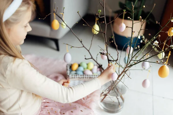 Niña caucásica feliz niño de ocho años en casa en la sala de estar con huevos de Pascua de colores. Permanecer en casa durante la pandemia del Coronavirus covid-19 — Foto de Stock