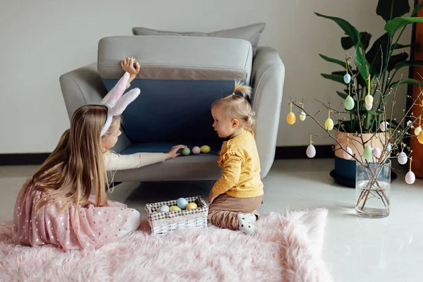 Heureuse fille caucasienne tout-petit de huit ans et sa petite sœur d'un an à la maison dans le salon avec des œufs de Pâques de couleur. Restez à la maison pendant la pandémie de Coronavirus covid-19 — Photo