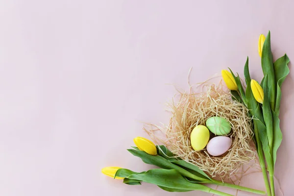 Stylish background with colorful easter eggs isolated on pastel pink background with yellow tulip flowers. Flat lay, top view, mockup, overhead, template