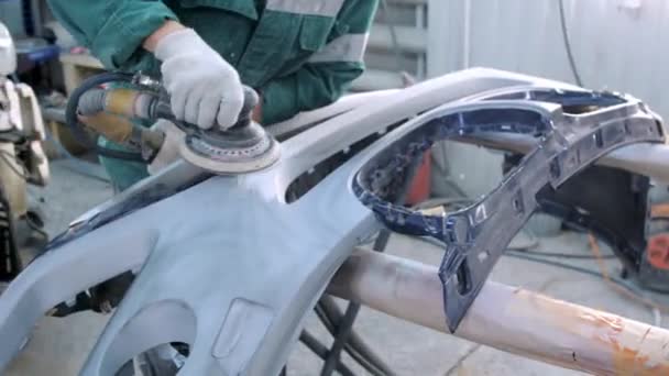 Worker sands bumper surface standing in car service garage — Stock Video