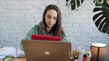 Dizüstü bilgisayarında yazı yazan gözlüklü ciddi bir beyaz kız öğrenci ders hazırlıyor.