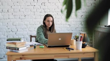 Dizüstü bilgisayarında yazı yazan gözlüklü ciddi bir beyaz kız öğrenci ders hazırlıyor.