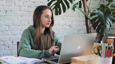 Dizüstü bilgisayarda yazı yazan ciddi bir beyaz kız öğrenci ders hazırlıyor.