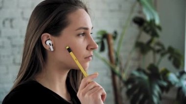 Kurumsal Kadın düşünüyor ve elinde bir kalem tutuyor kulaklıkla yan tarafa bakıyor. Kadın yukarıdaki aydınlatma odasına bakar gibi düşünüyor. Yakın plan. Yavaş çekim