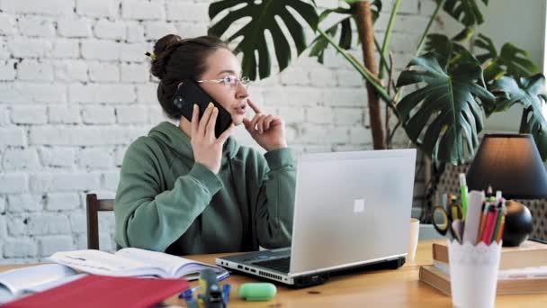 Blanke vrouw in bril werken vanuit huis en praten aan de telefoon tijdens het typen op de computer — Stockvideo