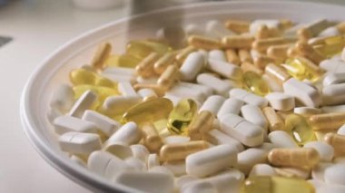 Kapsüllü ve tabletli farklı haplar beyaz tabaka, beyaz masa, tıbbi tedavi konsepti, yavaş çekim. Yakın plan.