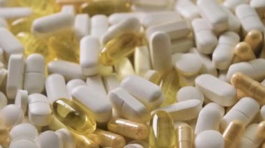 Kapsülleri ve tabletleri beyaz masaya düşen farklı haplar, tıbbi tedavi konsepti, yavaş çekim. Yakın plan.