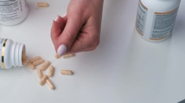 Ağır çekim. Kadın yumruğunu haplarla açıyor, beyaz arka planda balık yağı omega-3. Yakın plan.. 