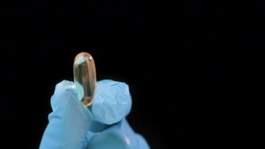 Kadınlar, elleri mavi tıbbi eldivenle sıkıca kavrulmuş avuç içi hapları, siyah arka planda jel kabuklu kapsüller. Omega 3, Multivitaminler, Kalsiyum, Antibiyotikler. Sağlık, karmaşık vitaminler. Sağlık