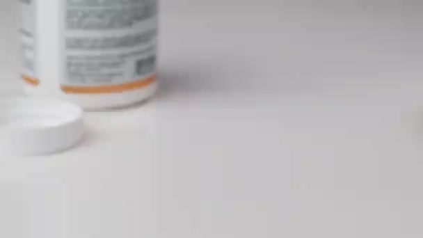 SLOW MOTION: een glazen pot valt en gele tabletten vallen eruit op een witte matentafel — Stockvideo