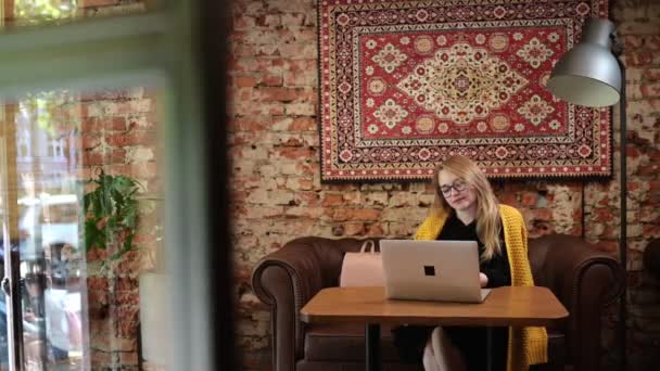 Νεαρή γυναίκα ανεξάρτητος συνεργάζεται με το φορητό υπολογιστή σε καφέ δακτυλογράφησης χαμογελώντας κάθεται στο τραπέζι μόνο με φορητό υπολογιστή. Αντίληψη των ανθρώπων και της σύγχρονης τεχνολογίας. — Αρχείο Βίντεο