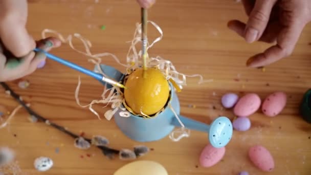 Meisje en moeder schilderen met Pasen gele eieren. Kind van Europees uiterlijk, decor op tafel. Gelukkige familie maakt decoraties voor Pasen en gekleurde eieren voor de vakantie. Een close-up. Bovenaanzicht. 4K — Stockvideo