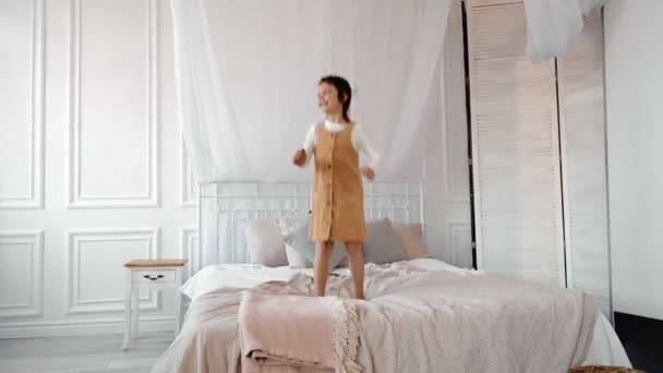 Rolig bedårande glad unge brunett flicka hoppa i säng, söt liten barn har kul dans till musik som spelar i sovrummet ensam njuta låtsas sångare på morgonen — Stockvideo