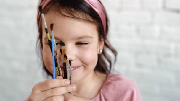 美しい少女は、カメラのレンズに筆で描く。かわいいブルネットの子供とそばかす。茶色の目。閉じろ! — ストック動画