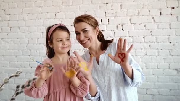 Fiatal anya és barna lánya boldog mosolygott és festett tenyereket festékkel. — Stock videók