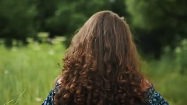 Veselá dívka s krásnými dlouhými kudrnatými vlasy běží a dívá se do kamery, pohled zezadu, Zpomalený pohyb — Stock video