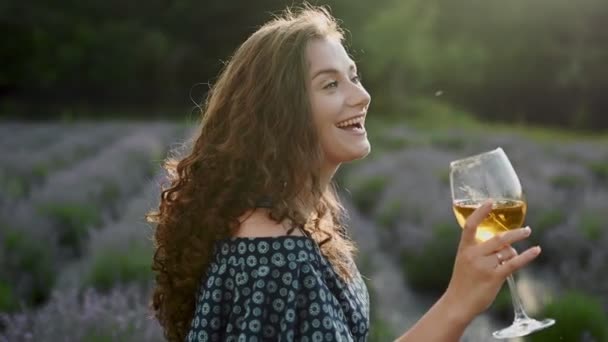 Cheerful caucasian woman in dress holding glass of wine on field outdoors, satisfied with sunny day vacations on city, Slow motion — ストック動画