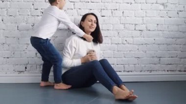 Mutlu hafta sonları. Mutlu çocuklu genç anne yatakta oynuyor ve kızıl gri kedi yatağın içinde yatıyor.