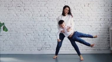 Mutlu aile sevdalısı genç anne kucağında sevimli, komik, küçük bir kız çocuğu ile kanepede oturur, neşeli bir anne kucağında küçük bir kız çocuğu taşır ve birlikte uçar gibi yapar.