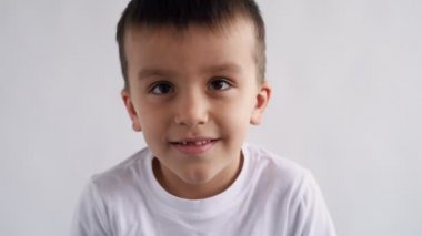 Yakından kahverengi gözlü çocuk kameraya bakıyor, beyaz arka planda duygusal olarak gülümsüyor, 4.