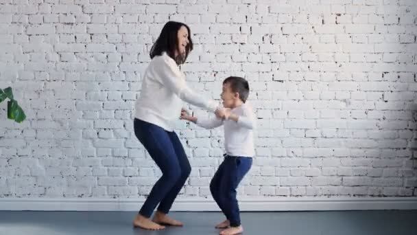 Active young mom babysiter and cute little kid son jumping dancing in modern house living room, happy family mother with child girl having fun enjoy playing funny activity together at home — ストック動画
