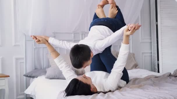 The kid, a boy, plays with her mother at home, laughs and flies like an airplane in her mothers arms. Child, young mother doing morning exercises together. Happy family doing gymnastics on the bed — стоковое видео