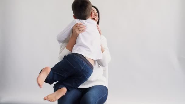 Hermosa mujer feliz sonriente amorosa sentada sobre fondo blanco y abrazando a su hijo que corre hacia ella con caras felices 4k — Vídeos de Stock