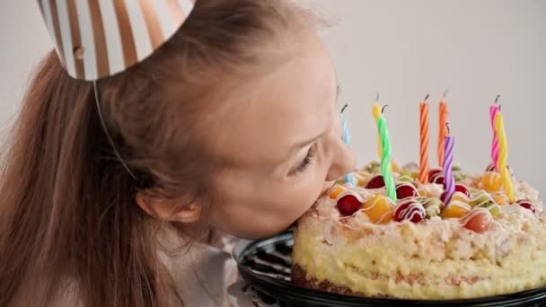 A happy child bites a big cake at a table on a light background. A funny little girl eats a delicious a dessert. Slow motion — Stockvideo